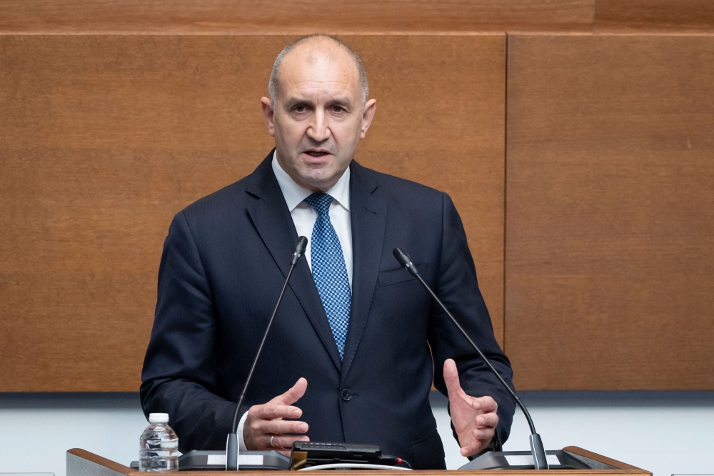Bulgarian Prime Minister Rumen Radev speaks at a press conference, with the Bulgarian flag visible.